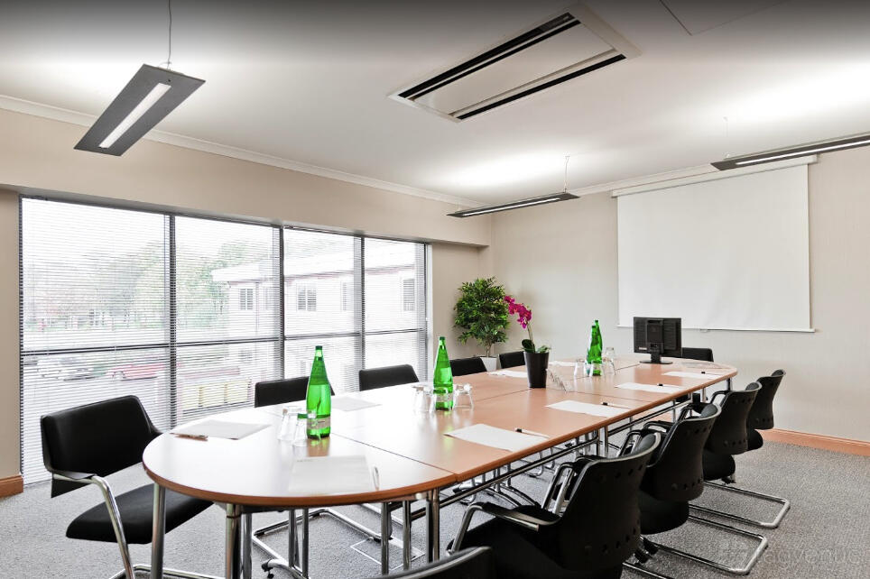 A meeting room with a long conference table, black chairs, bottled water, and large windows at Biz Hub City View House.