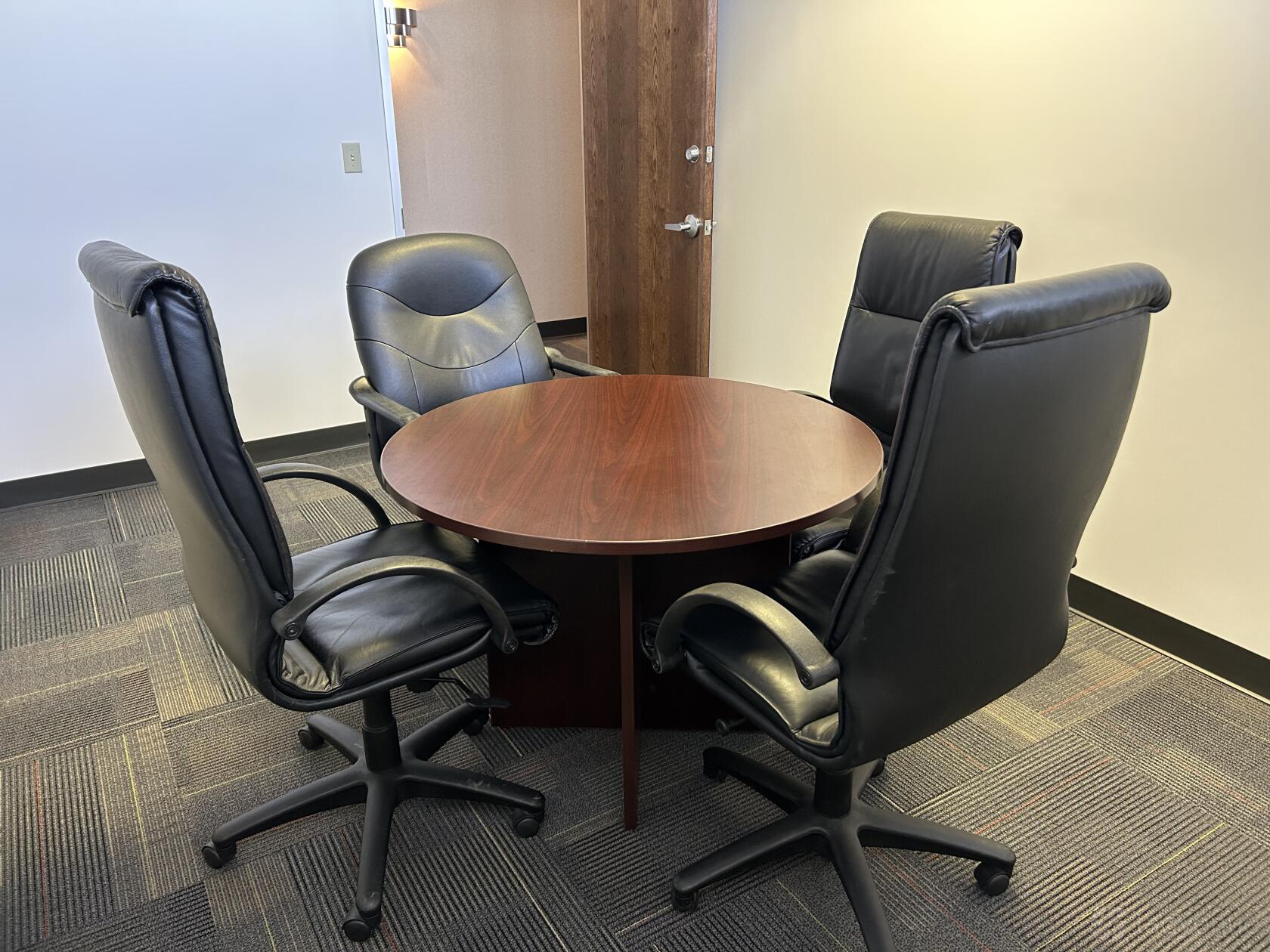 A coworking space with a round wooden table and four black leather chairs at Executive Workspace Trinity Centre.