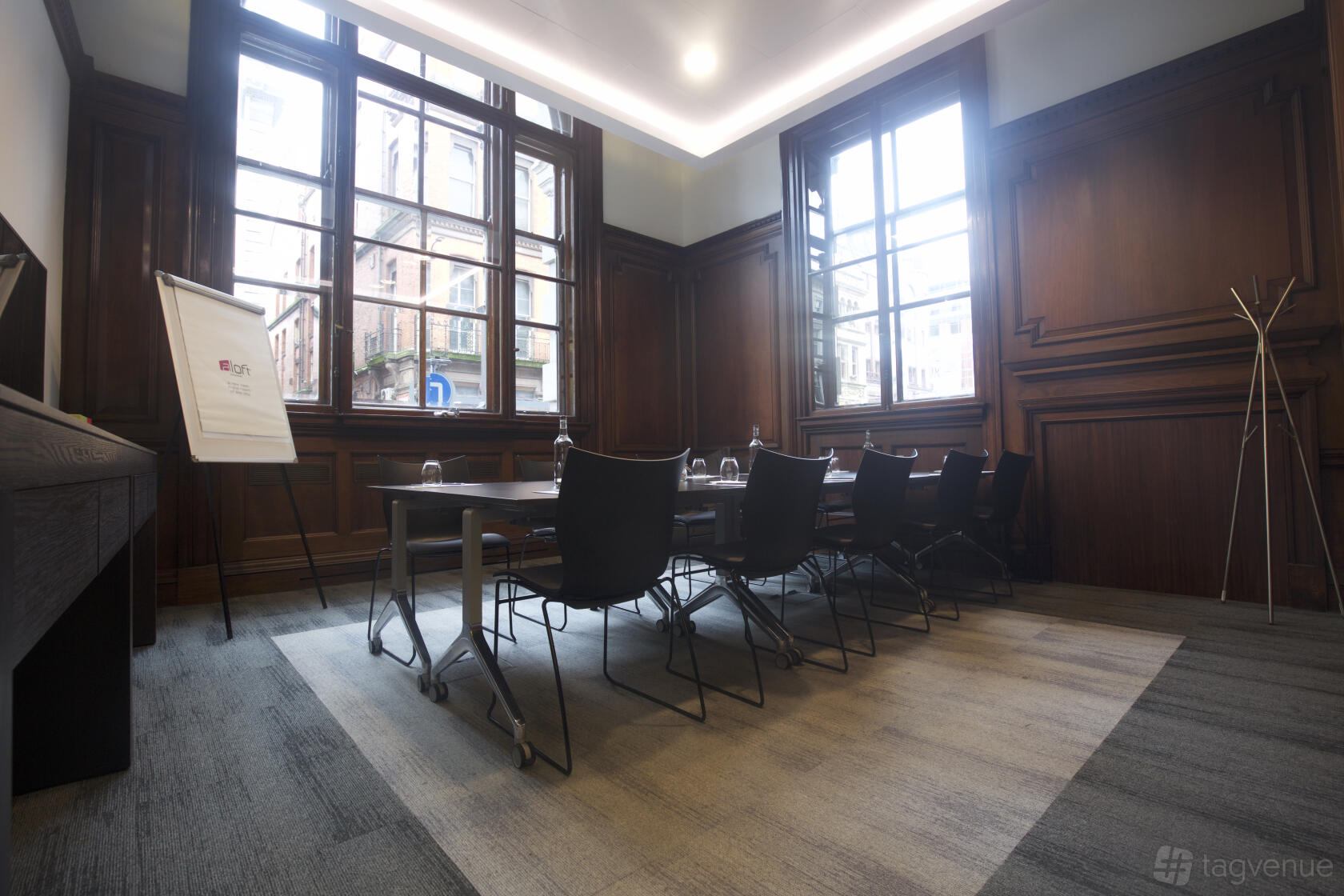A meeting room with high ceilings, large windows, dark wood paneling, and a rectangular table at Aloft Liverpool.