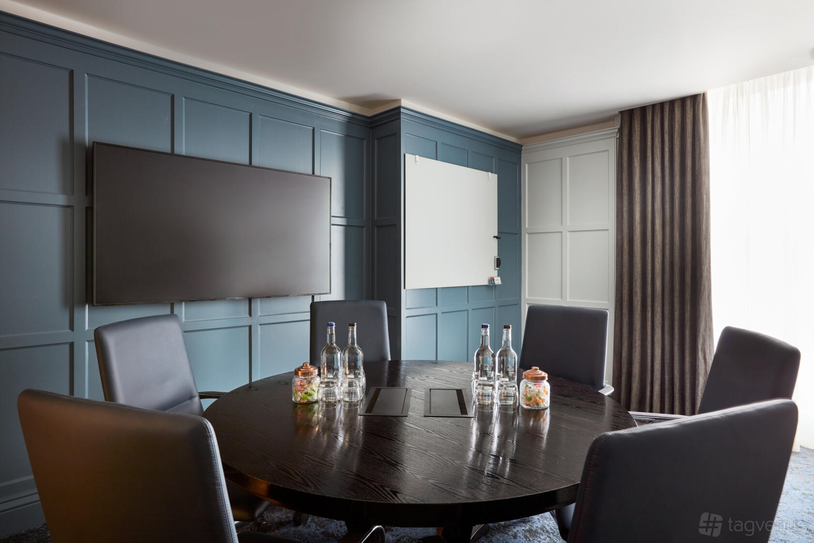 A hotel boardroom with a round dark wood table, leather chairs, large screen, and floor-to-ceiling windows at The Clermont Victoria.