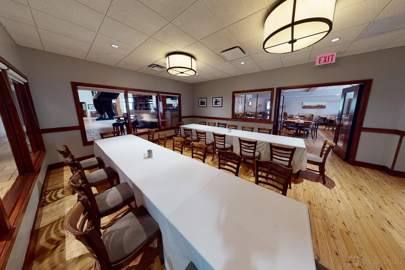 A dining room with long tables covered in white linens, wooden chairs, and large round ceiling lights at Pinstripes - South Barrington.