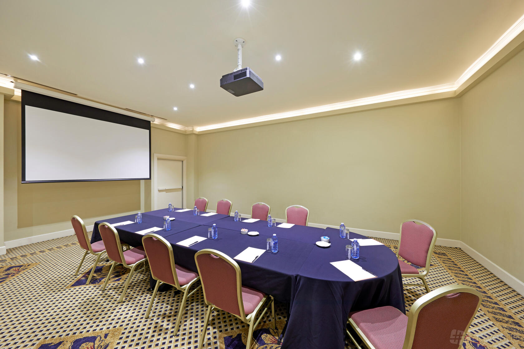 An event space with U-shaped table setup, pink chairs, projector, and screen at Stamford Plaza Sydney Airport Hotel.