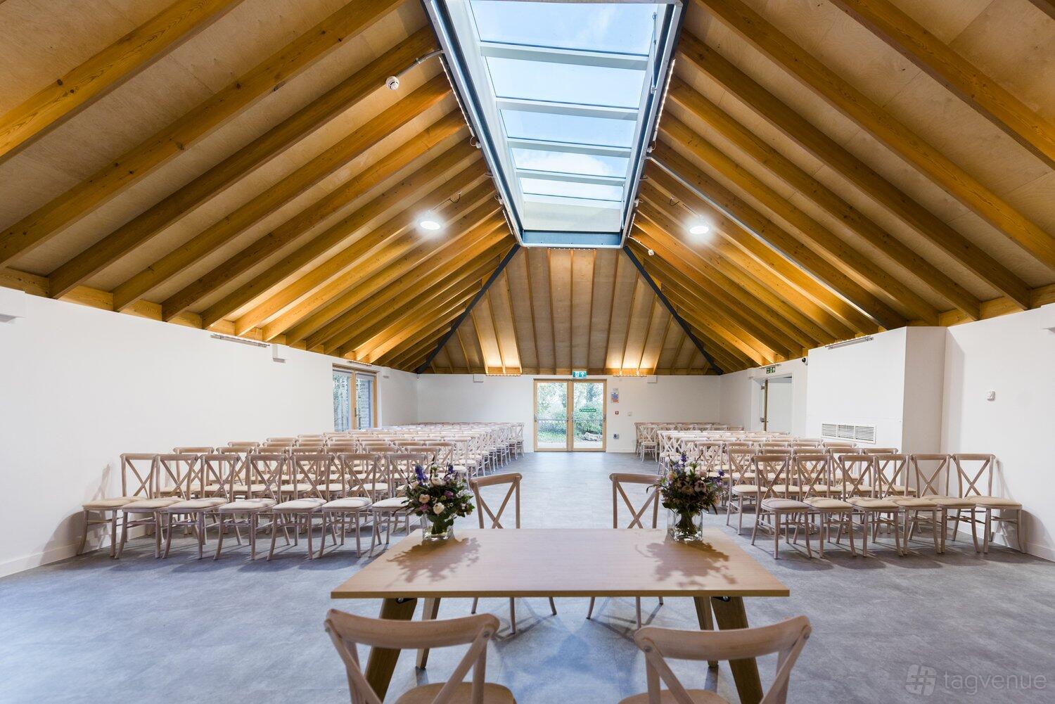 A function room with a vaulted wooden ceiling, skylight, and rows of chairs facing a table at The Glass House - Springfield Park.