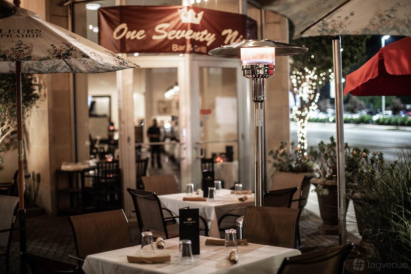 An outdoor restaurant patio with covered tables, umbrellas, and a standing heater at One Seventy Nine Bar & Grill.