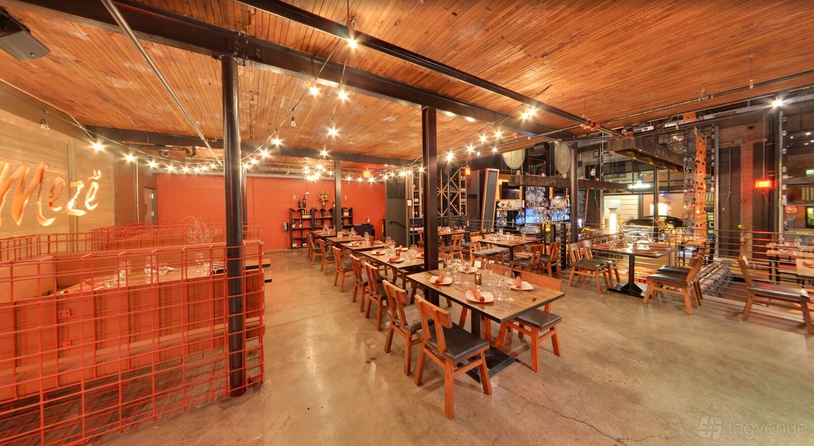 An event space in a restaurant with wooden ceilings, string lights, long wooden tables and open shelving at Meze Greek Fusion.
