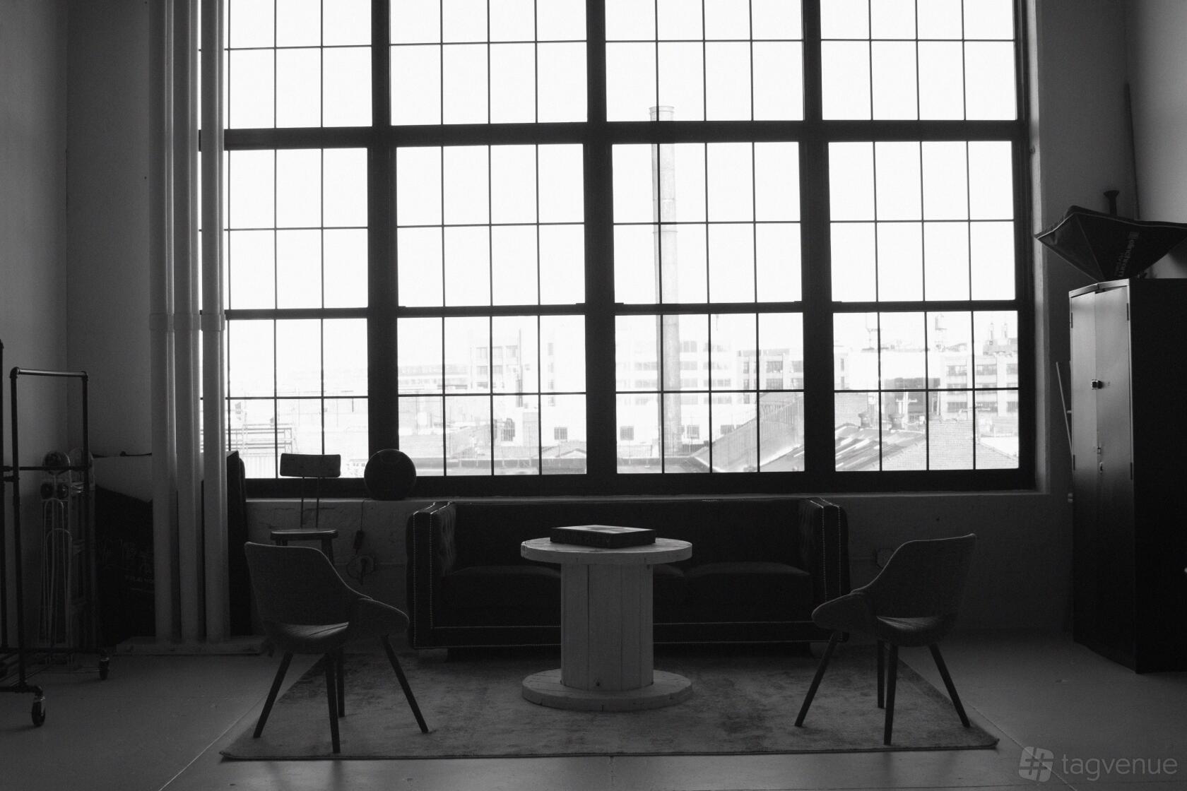 A loft with floor-to-ceiling industrial windows, a sofa, wooden table, and armchairs at Waverly Productions.