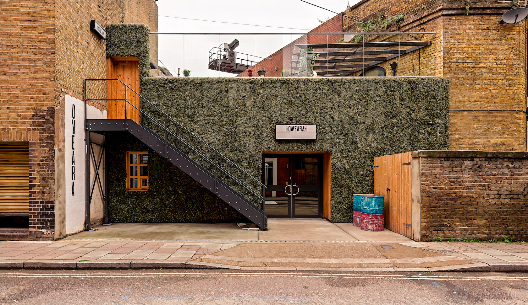 A versatile event space with a green wall exterior, metal staircase, and glass entrance at Omeara.