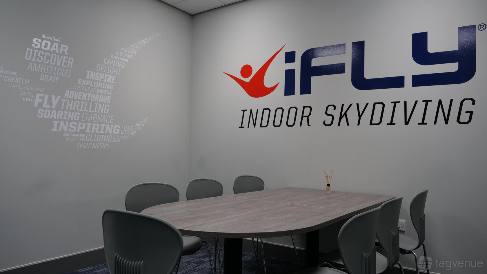 A meeting room with a rectangular wooden table, gray chairs, and wall branding at iFLY Indoor Skydiving at The O2.