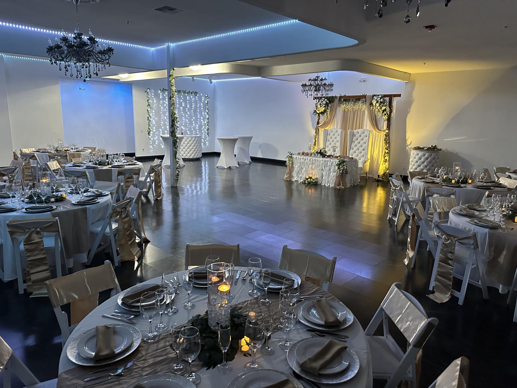 A ballroom with round tables draped in white linens, candlelit centerpieces, and a decorative sweetheart table at Vegas Event Space.