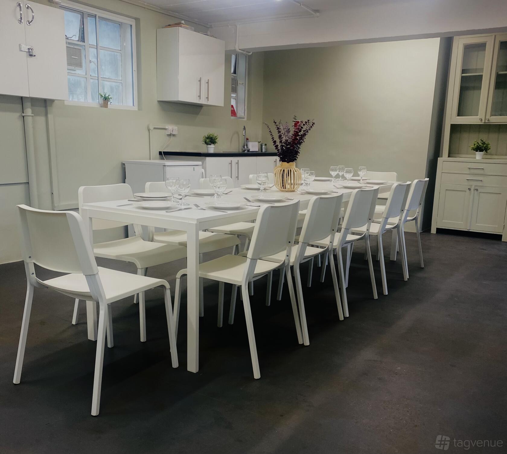A meeting room with a long white table, matching chairs, place settings, and a kitchenette at Sands End Arts & Community Centre.