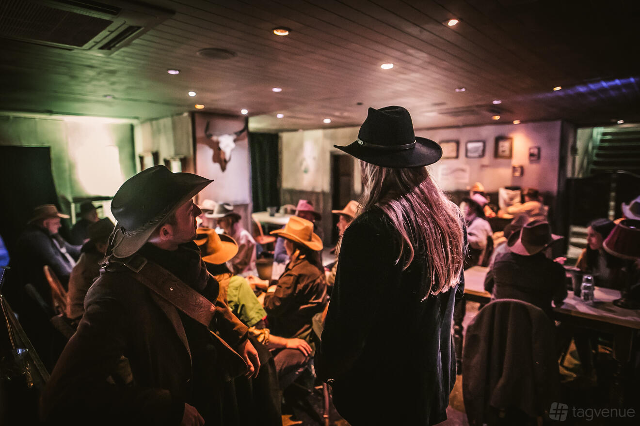 A cocktail bar with wooden ceilings, dim lighting, and guests in cowboy hats at Moonshine Saloon.