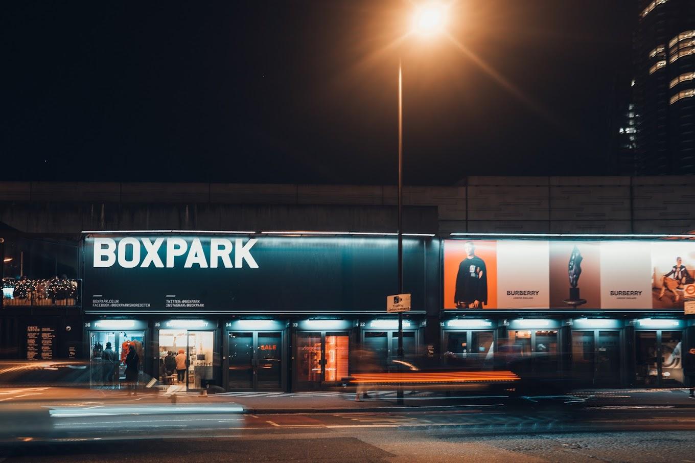 A restaurant with a black exterior facade and illuminated signage at Boxpark Shoreditch.