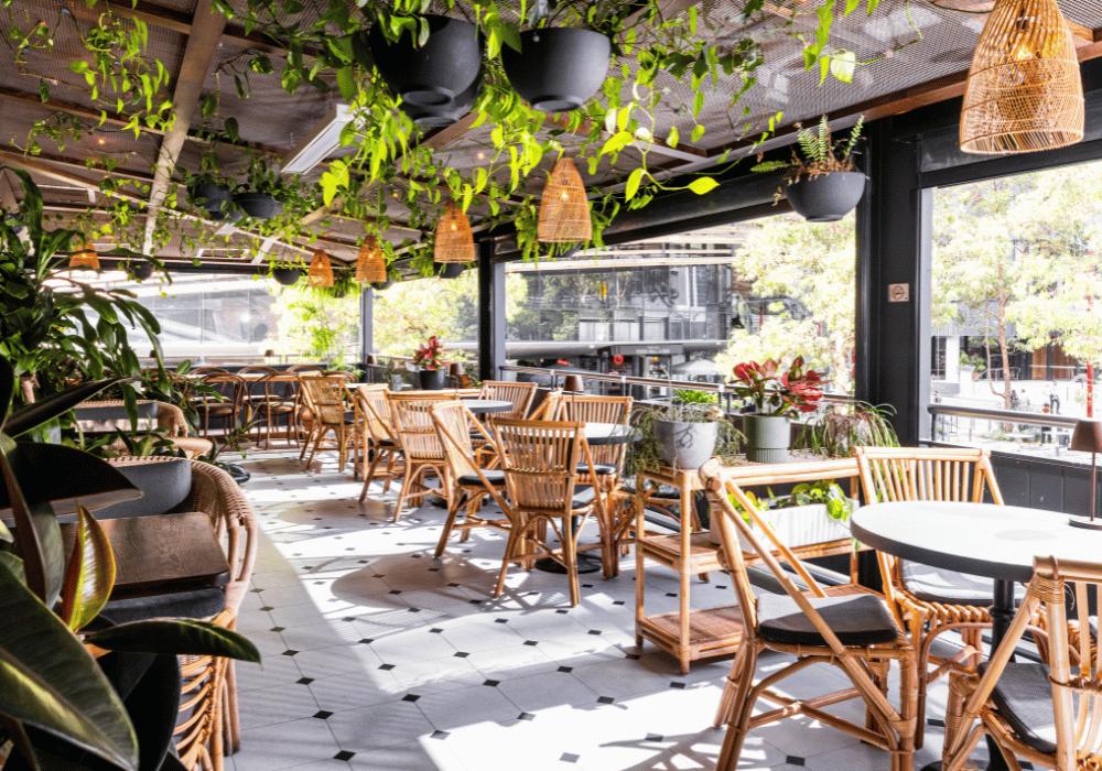 A pub terrace with rattan chairs, round tables, hanging plants, and natural light at Pumphouse Sydney.