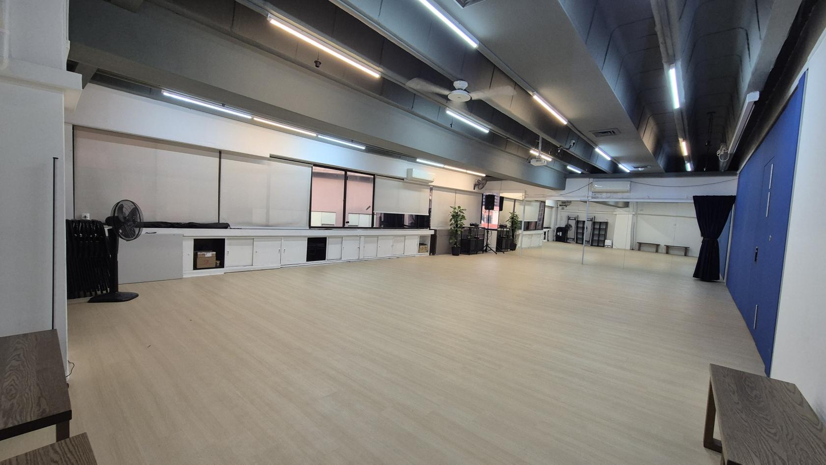 A dance studio with light wood floors, wall mirrors, storage cabinets, and ceiling fans at Caliente Venues @ Bugis Midland House.