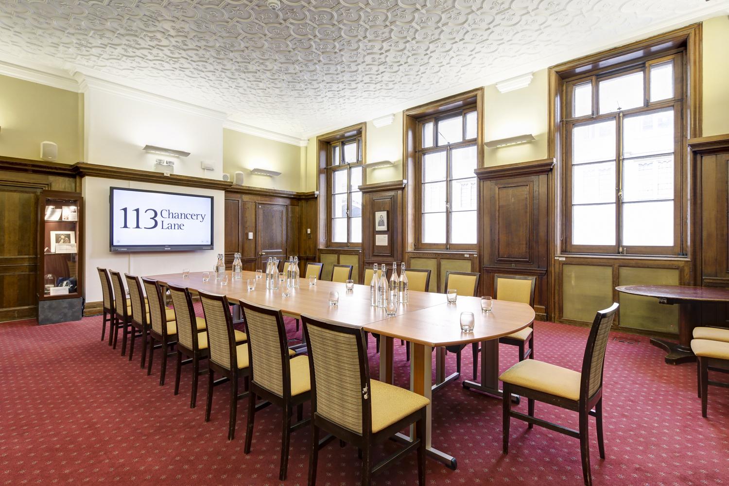 A function room with high ceilings, wood paneling, red carpet, and a long conference table at 113 Chancery Lane.