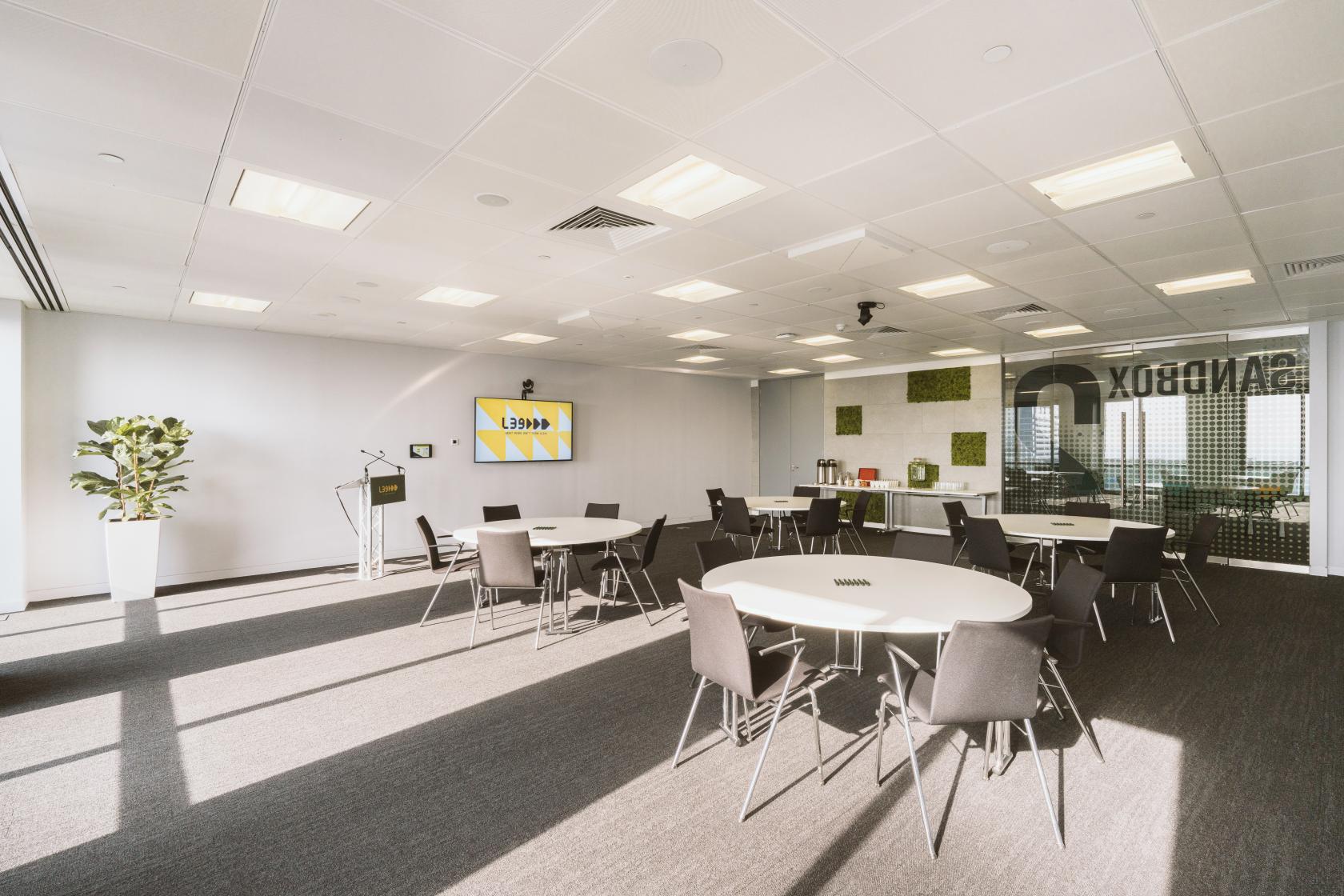 An event space with round tables, stackable chairs, large windows, and a digital display at Level39.