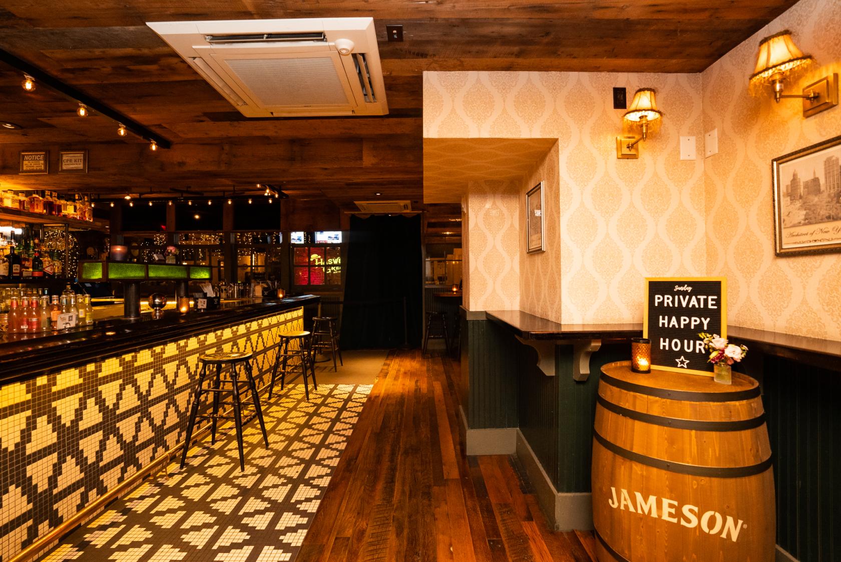 A bar in a restaurant with mosaic tile flooring, wooden accents, and a whiskey barrel at Haswell Green's.