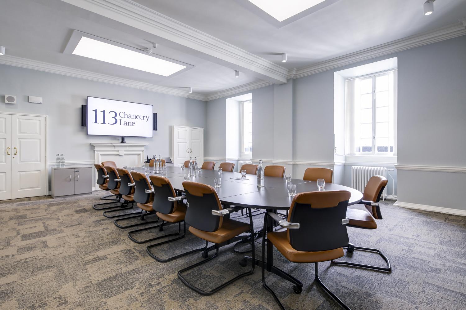 A meeting room with a long oval table, brown leather chairs, large windows, and a presentation screen at 113 Chancery Lane.