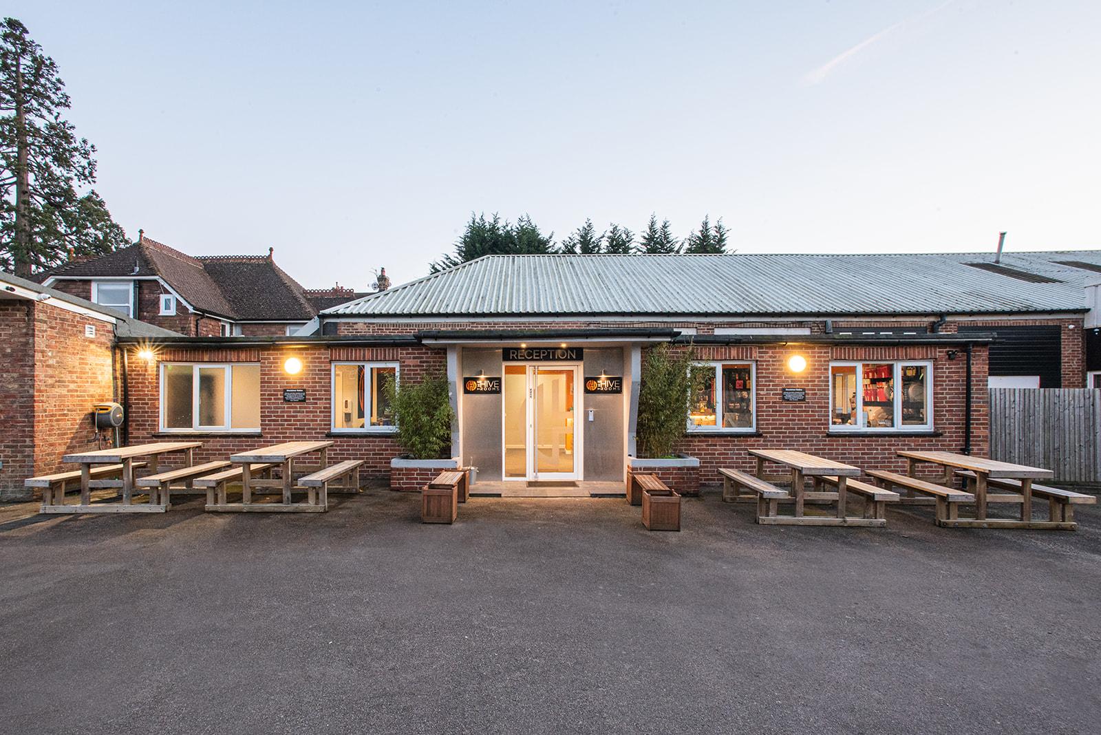 A recording studio with a brick exterior, metal roof, picnic tables, and exterior lighting at The Hive Rooms.