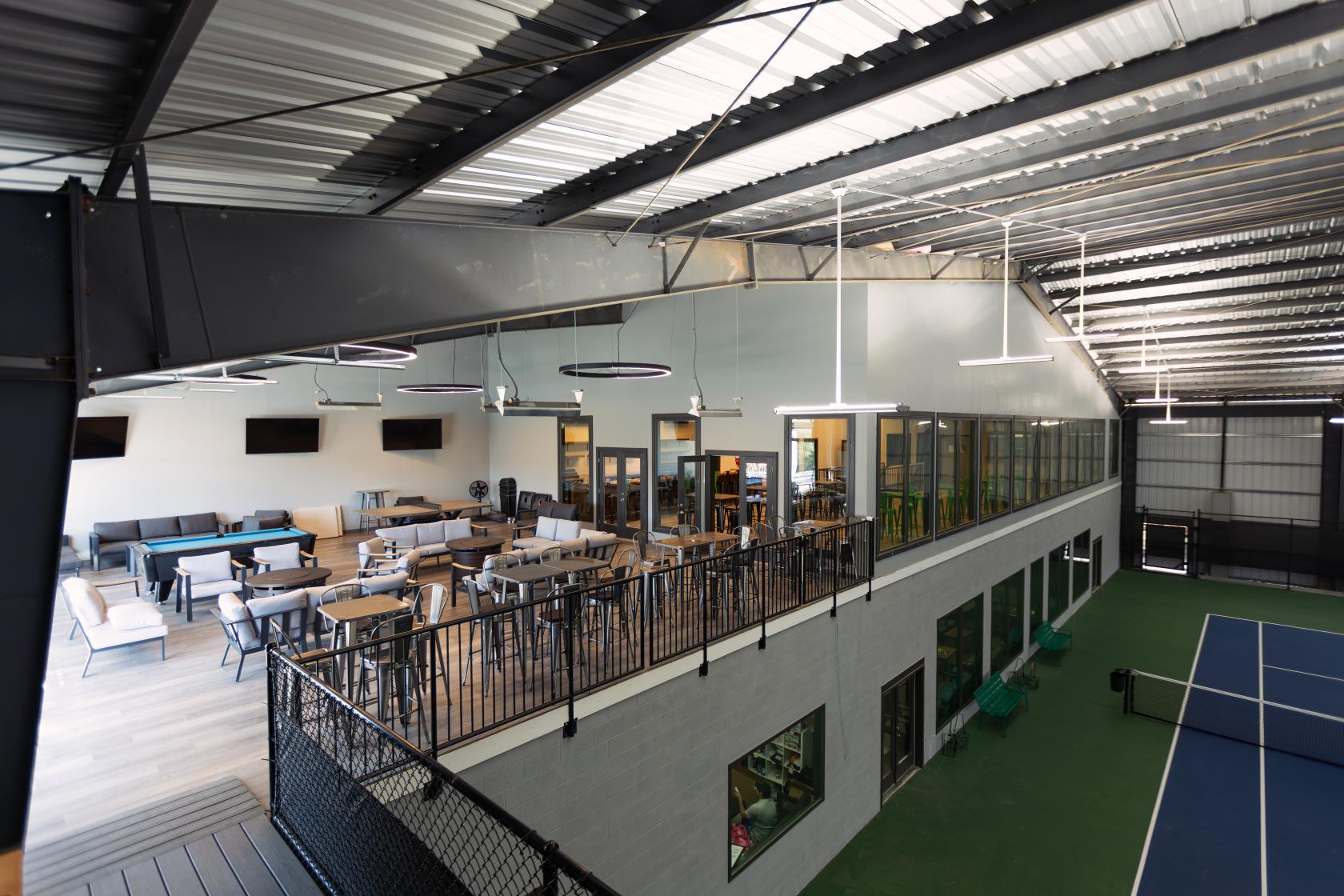 An event space with high ceilings, lounge seating, and tables overlooking indoor tennis courts at ITA Atlanta.