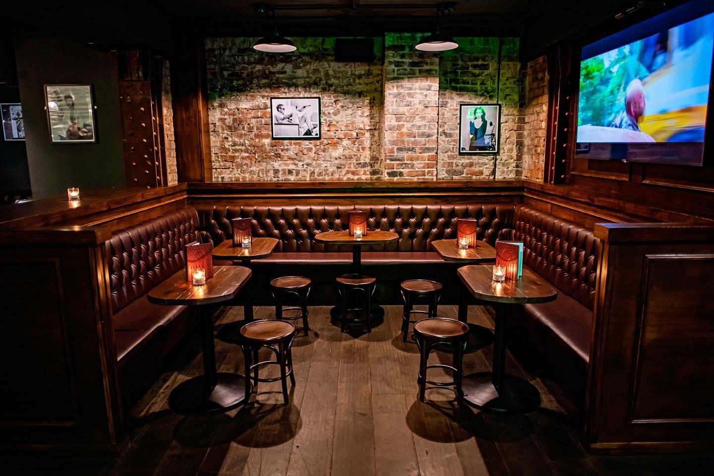 A bar with tufted leather booth seating, exposed brick walls, and framed photographs at Point Blank Shooting.