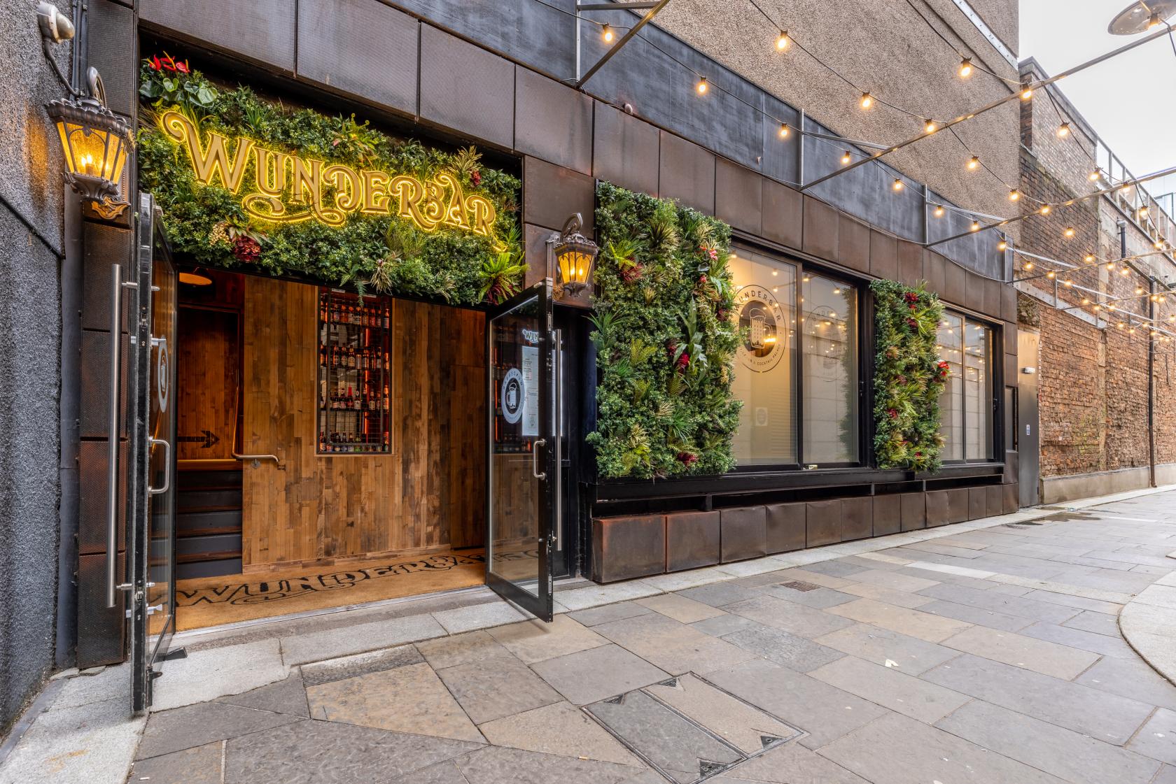 An exterior of a pub with greenery-covered walls, string lights, and decorative lanterns at Wunderbar City Centre.