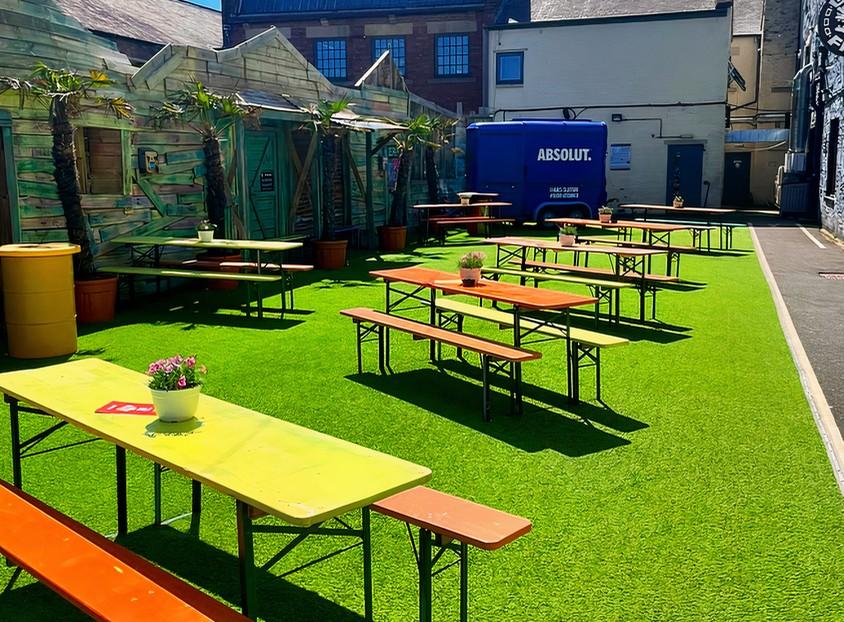 An outdoor bar terrace with colorful picnic tables on artificial grass and potted plants at Golf Fang Newcastle.