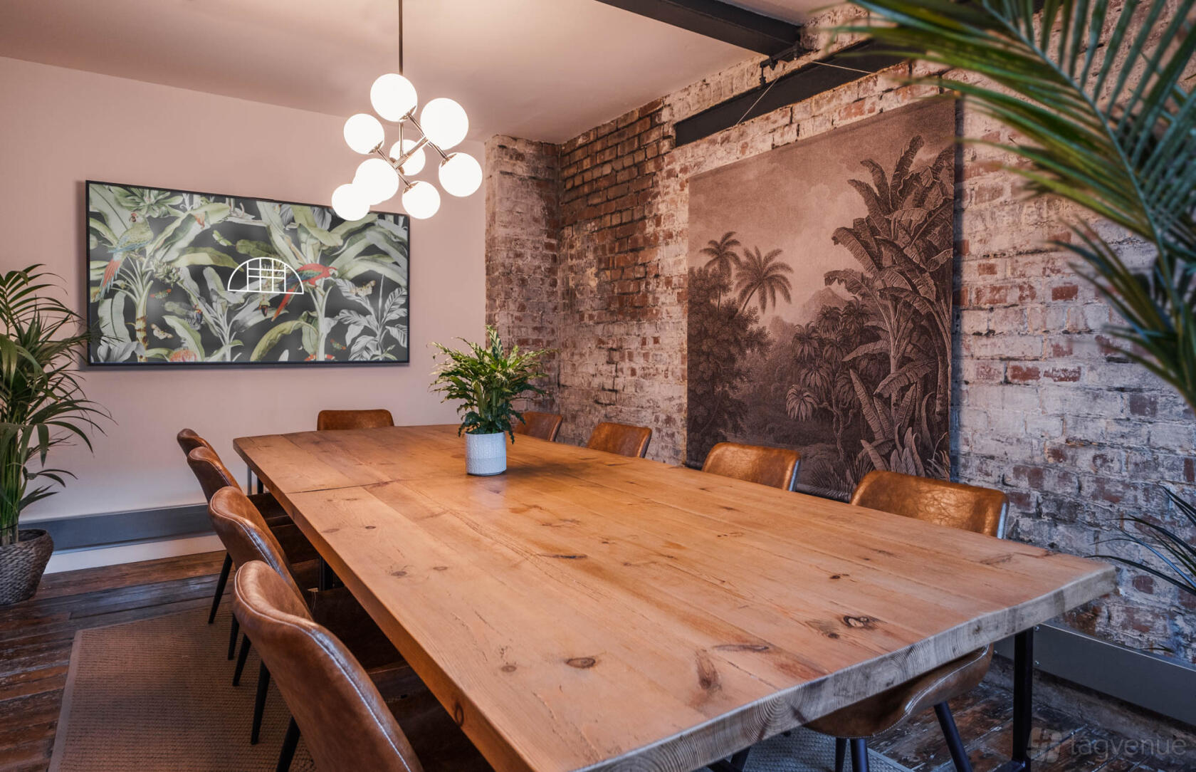 A meeting room with exposed brick walls, a large wooden table, leather chairs, and modern lighting at Beehive Lofts.