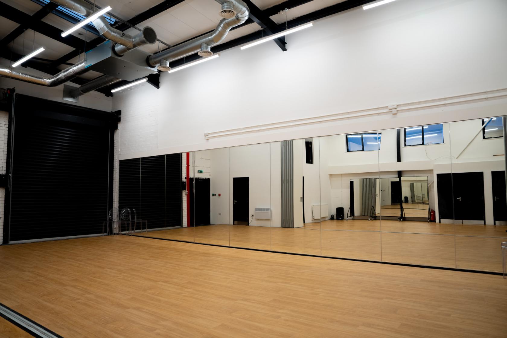 A dance studio with full-length wall mirrors, wood flooring, and exposed ceiling pipes at Eloquent Arts Centre.