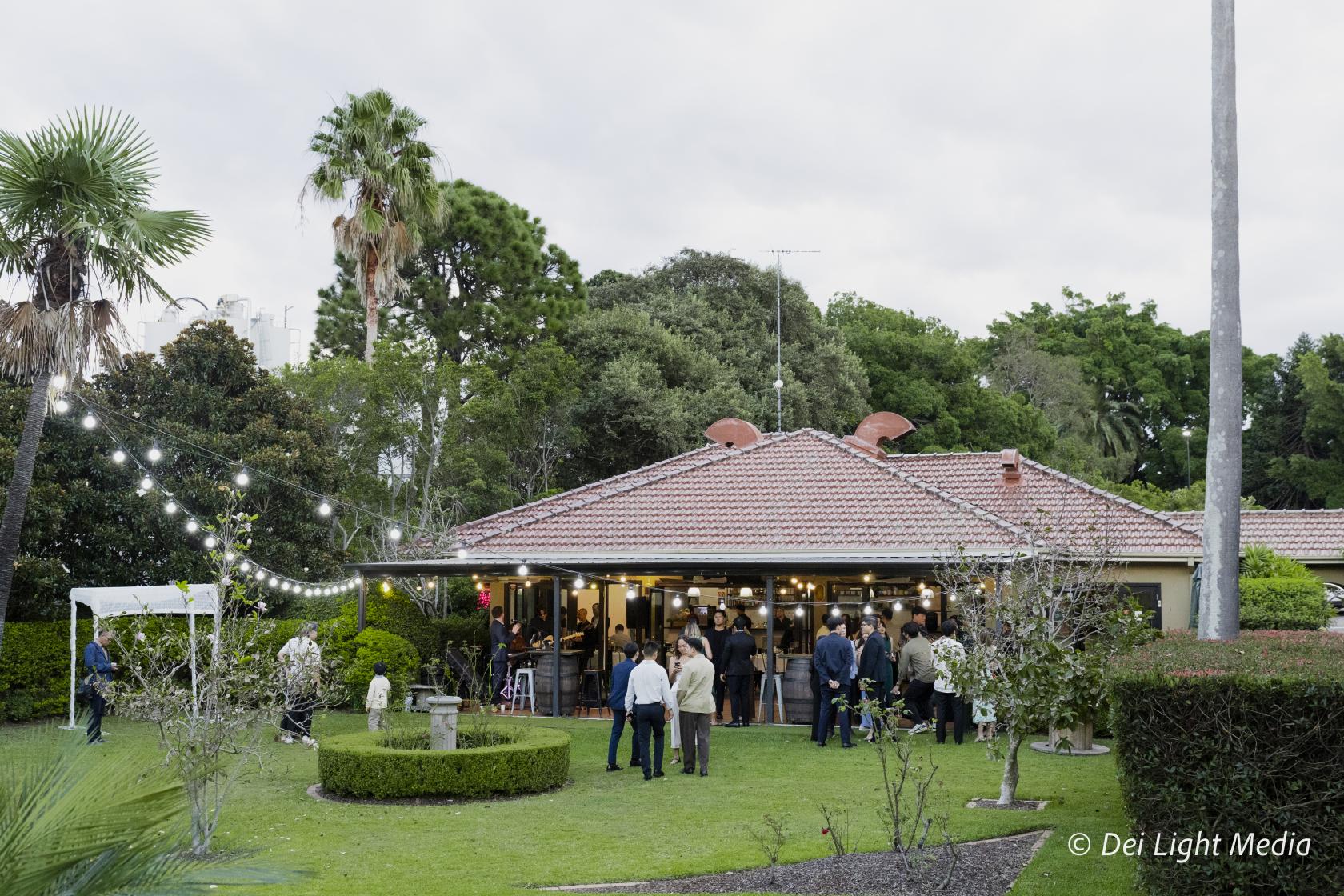 An event venue with a tiled roof, outdoor string lights, manicured hedges, and lawn gatherings at Will & Mike's.