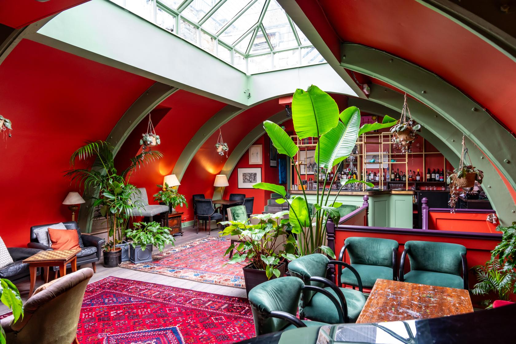 An event space in a restaurant with red arched walls, skylight ceiling, eclectic furniture, and lush plants at L'Escargot.