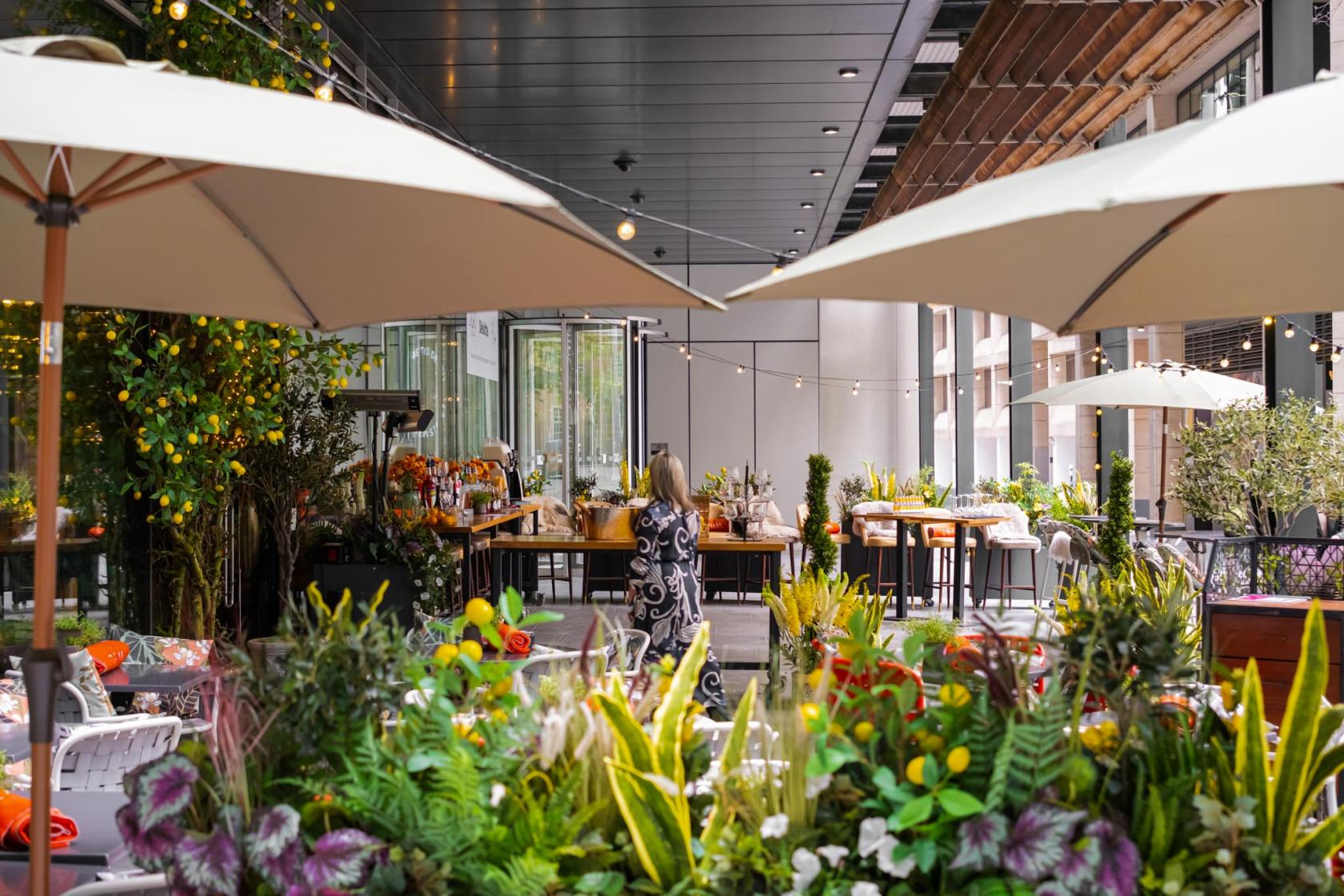 An outdoor cocktail bar with string lights, large umbrellas, and lush greenery at The Refinery New Street Square.