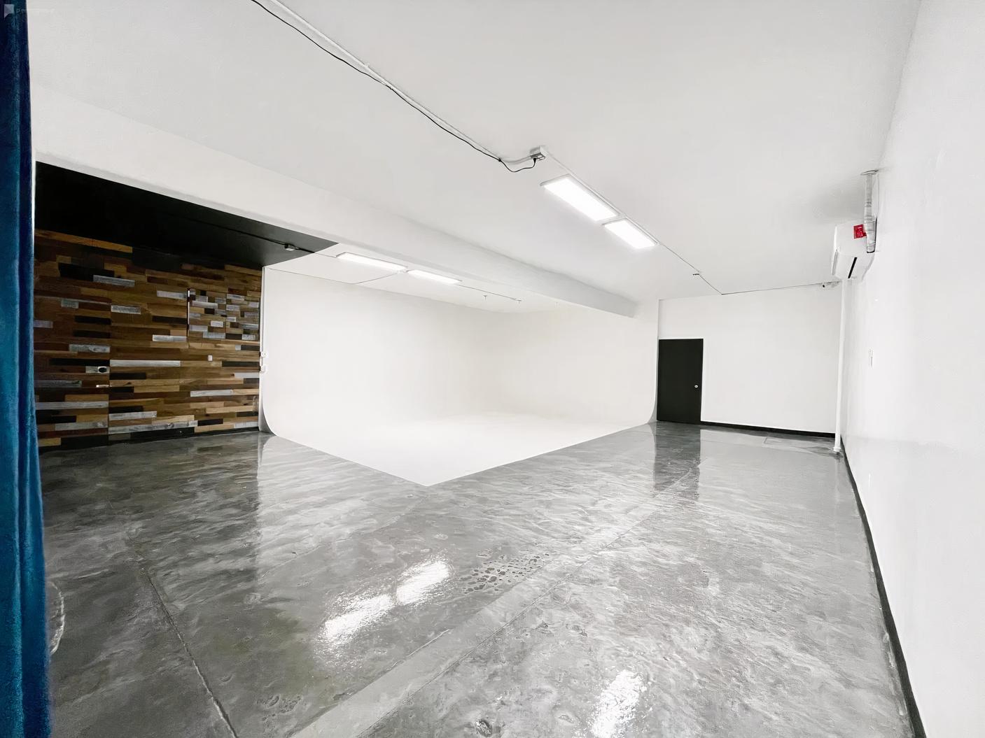 A photo studio with a large white cyclorama wall, polished concrete floors, and wood accent wall at Spekulor Cameras & Production.