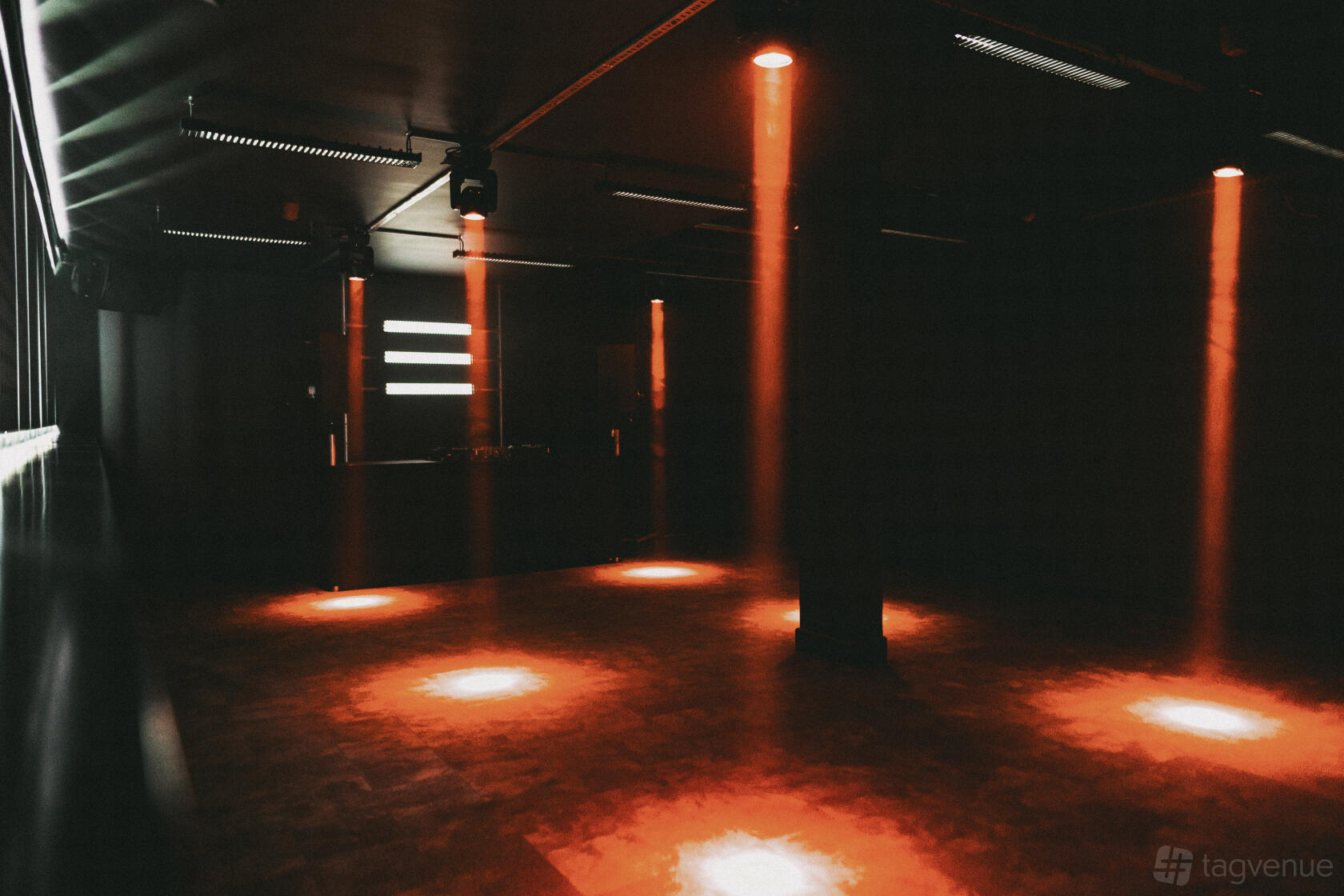 A nightclub event space with dark walls, a dance floor, and red spotlights at Bricks.