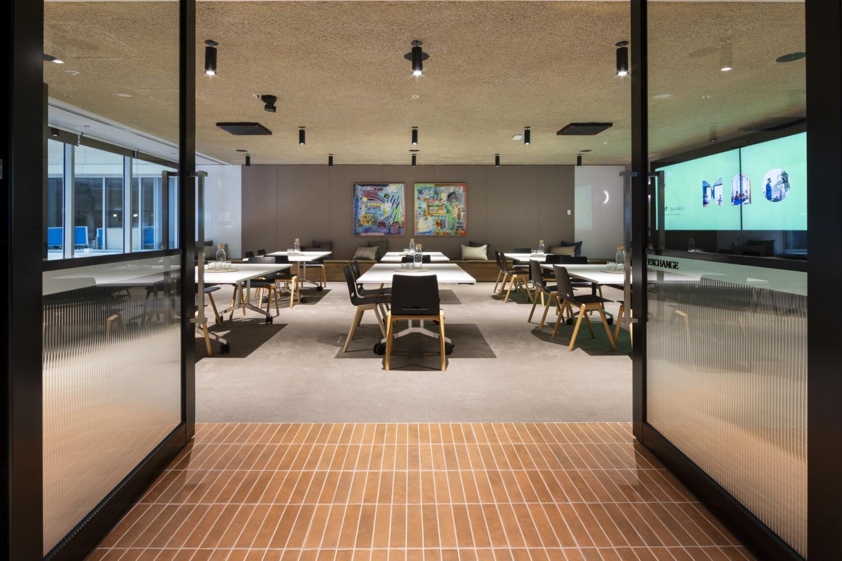 A meeting room with workshop tables, large digital screens, and modern art at Space&Co. 530 Collins Street, Melbourne.