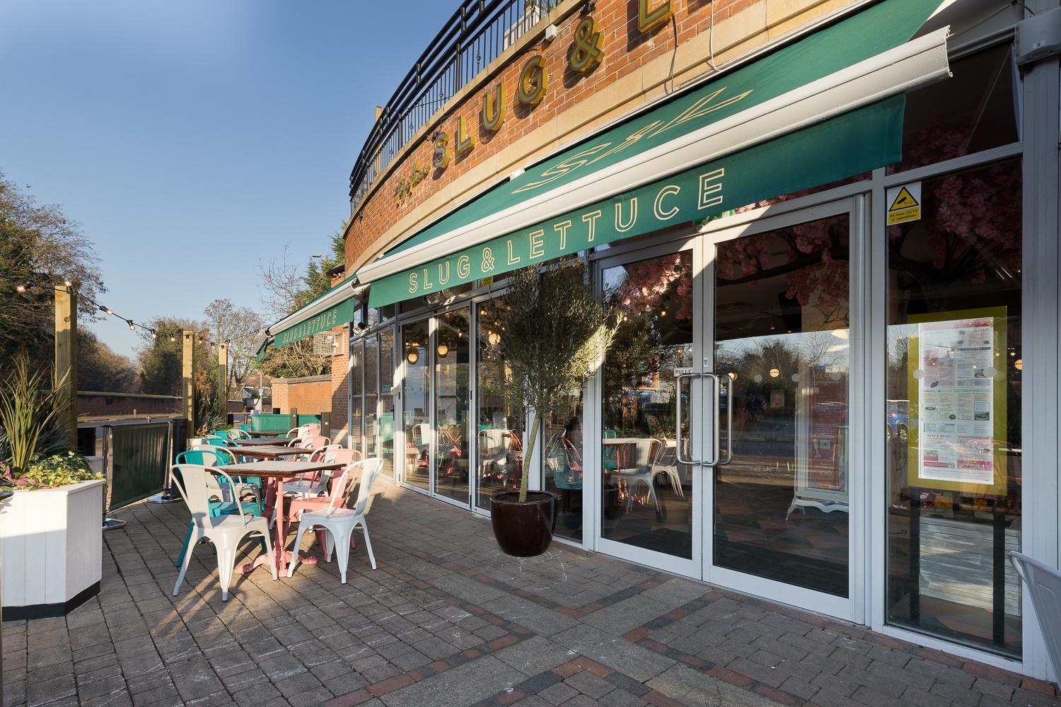 An outdoor seating area with colorful chairs and tables under a green awning at Slug and Lettuce, Didsbury.