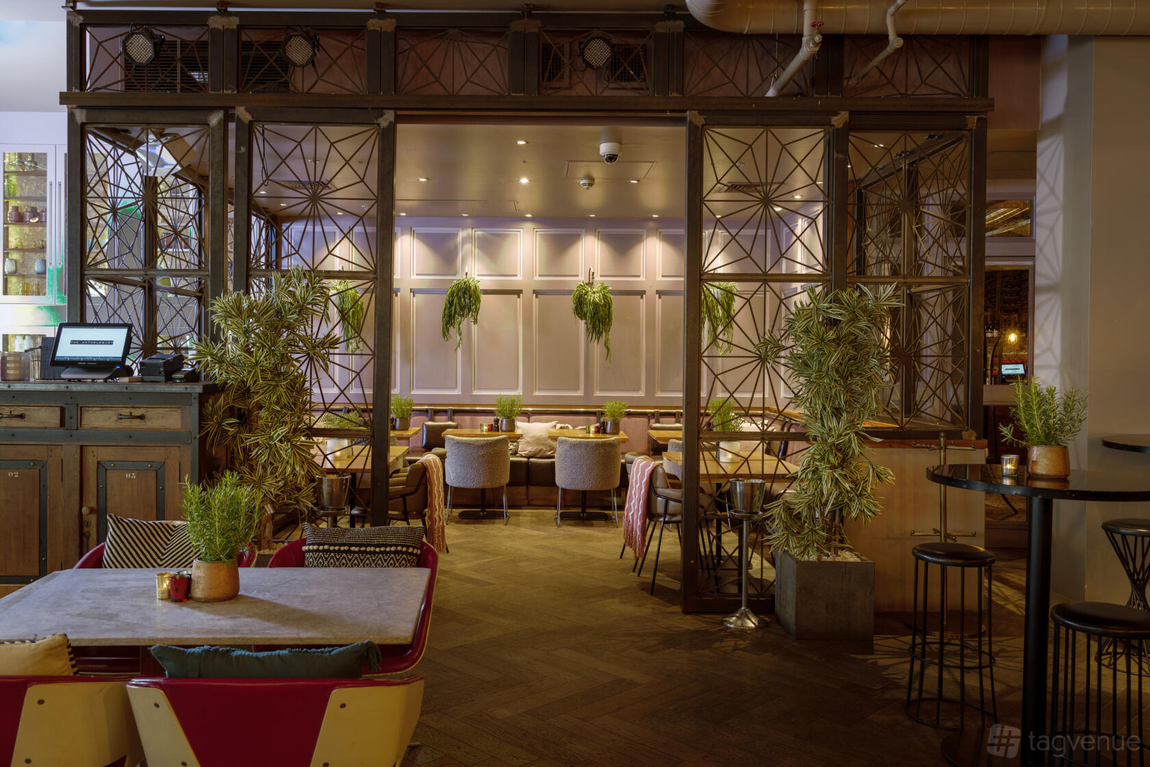 An event space with potted plants, soft armchairs, and decorative metalwork screening at The Anthologist.
