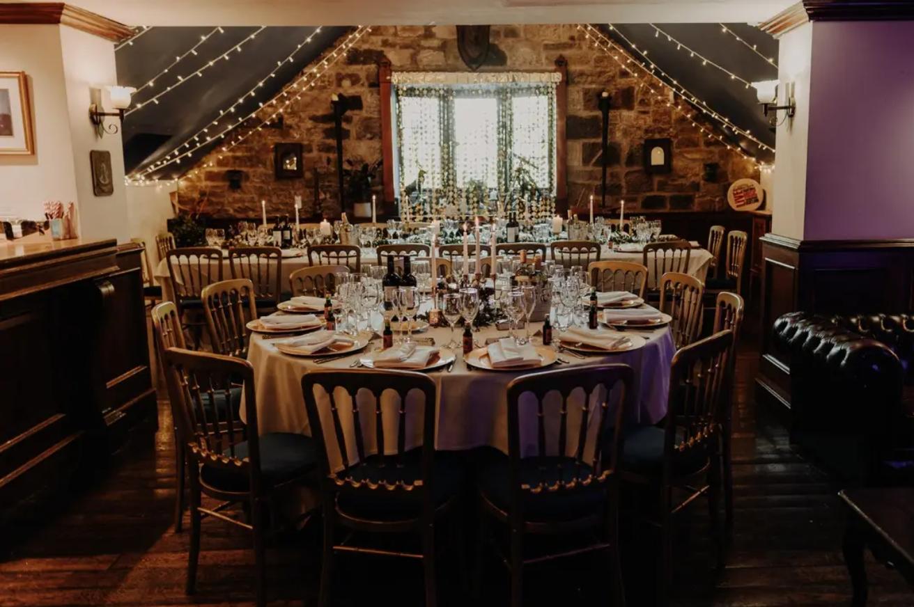 An event space in a pub with exposed stone walls, fairy lights, and round tables set for dining at Òran Mór.