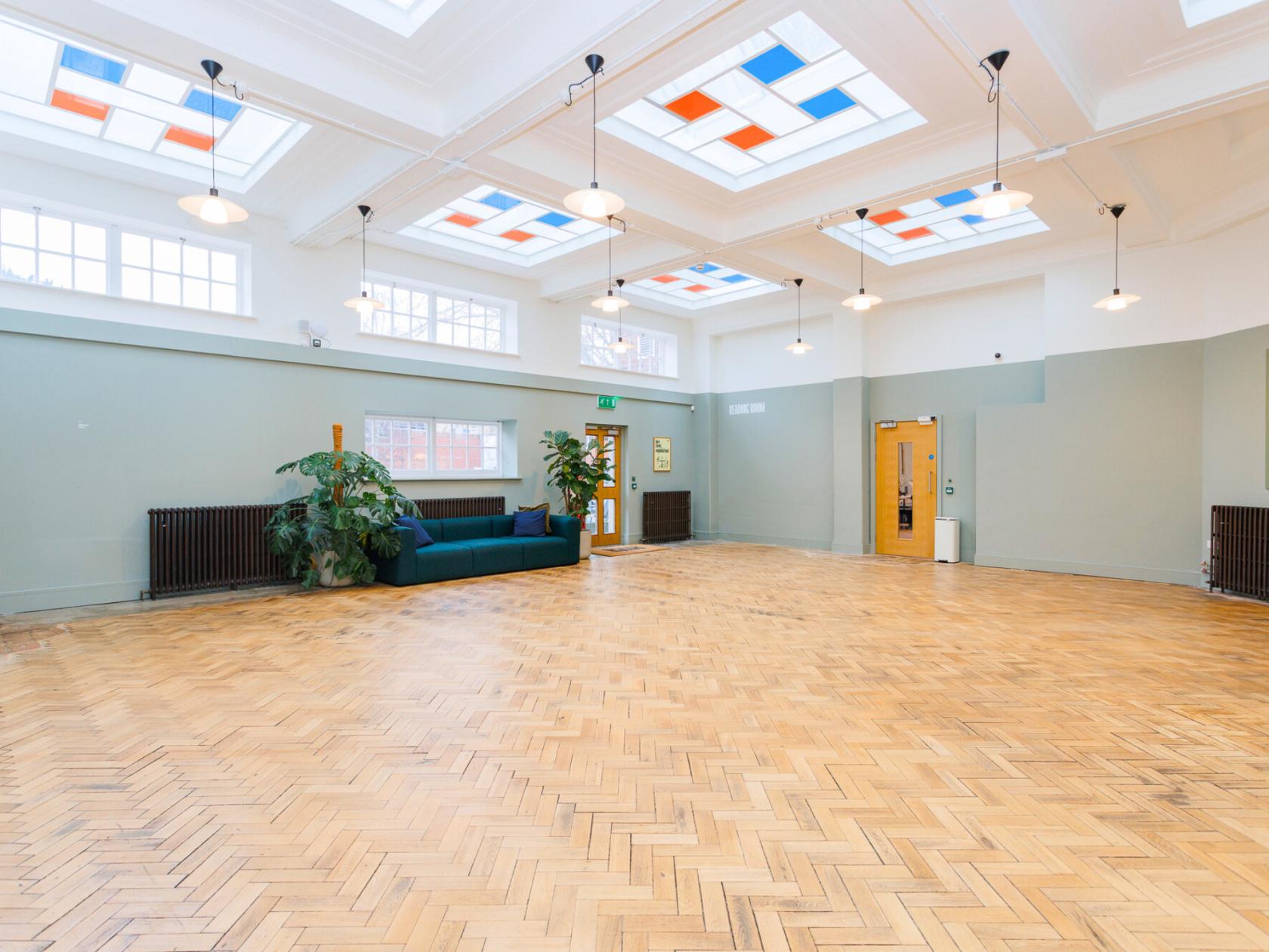 An event space with herringbone wood flooring, skylights, large windows, and a blue sofa at Patch High Wycombe.
