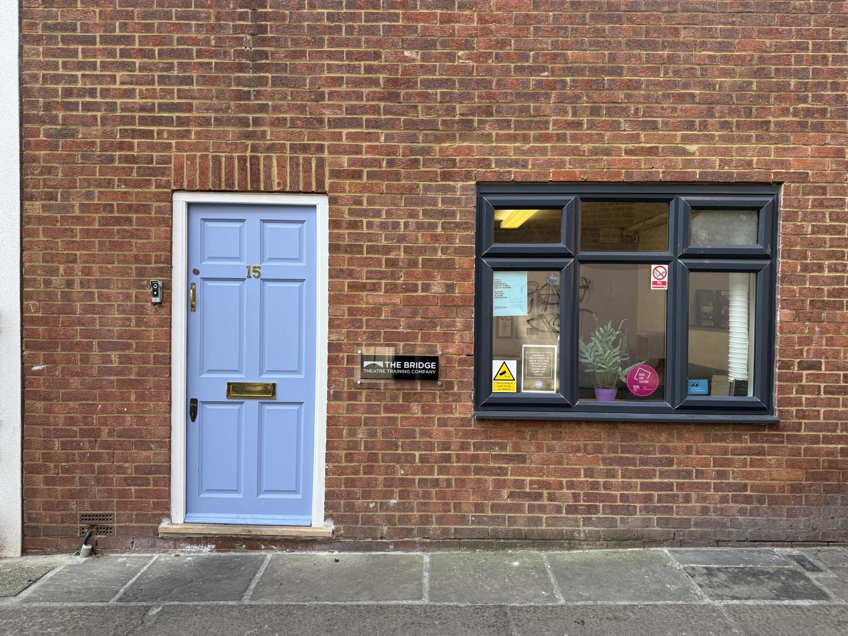 A brick exterior with a light blue door and large black-trimmed window at artsHouse.