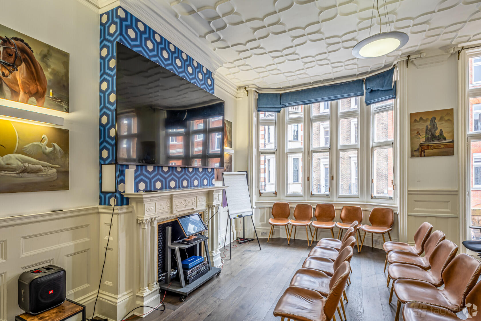 A meeting room with a wall-mounted TV, patterned fireplace, leather chairs in a semi-circle, and large windows at 54 Welbeck St W1G 9XS.