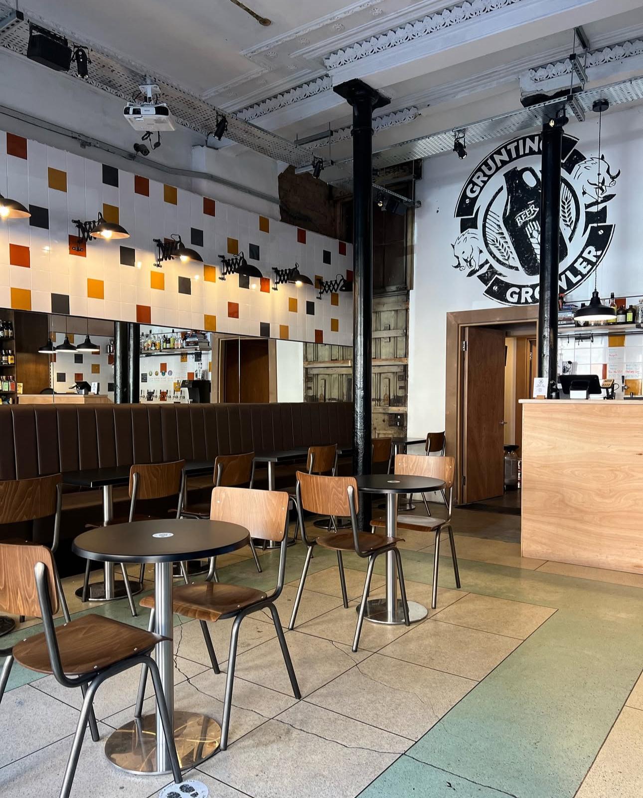 An event space in a bar with modern wall tiles, wood tables, and industrial lighting at Grunting Growler.