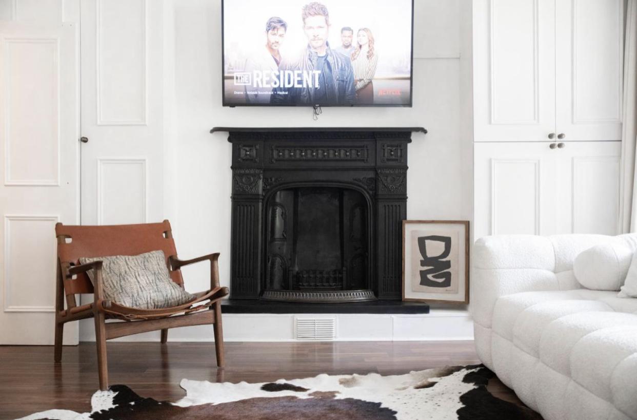 An apartment living area with a black cast iron fireplace, mounted TV, cowhide rug, leather chair, and white sofa at Victorian Notting Hill Flat.