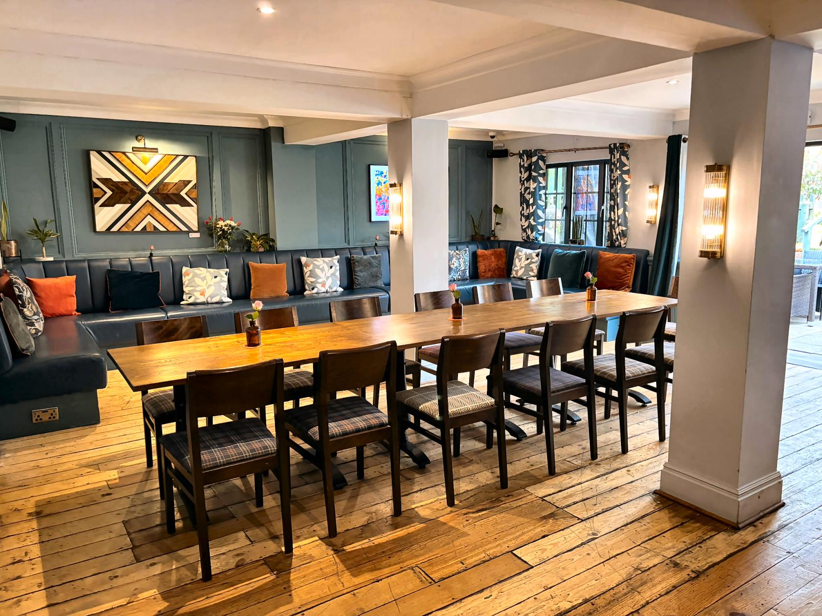 A meeting room with a long wooden table, cushioned bench seating, and wood floors at The Crown Inn at Burnham Beeches.