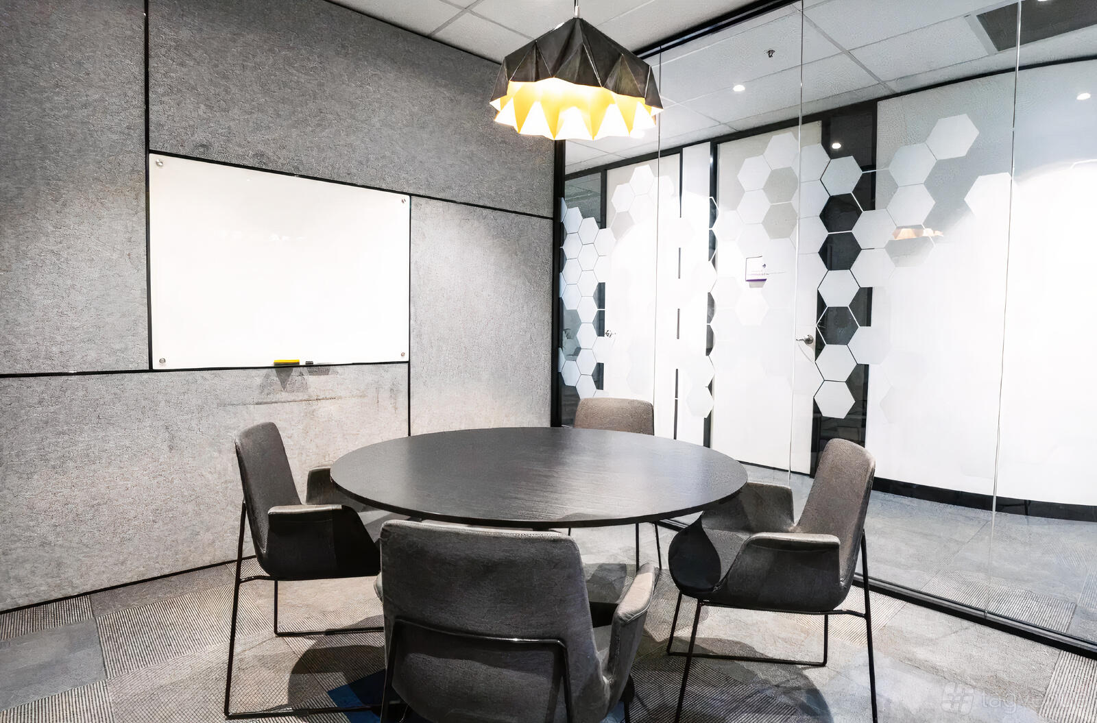 A meeting room with a round table, four grey chairs, a wall-mounted whiteboard, and hexagonal glass decals at Waterman at Narre Warren.