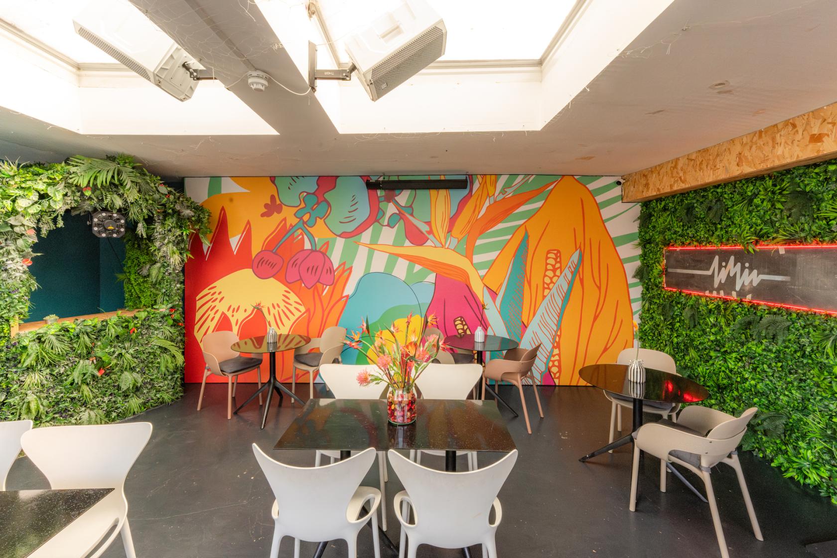 An event space in a restaurant with a colorful mural, skylight, and greenery at LIMIN SOUTHBANK.