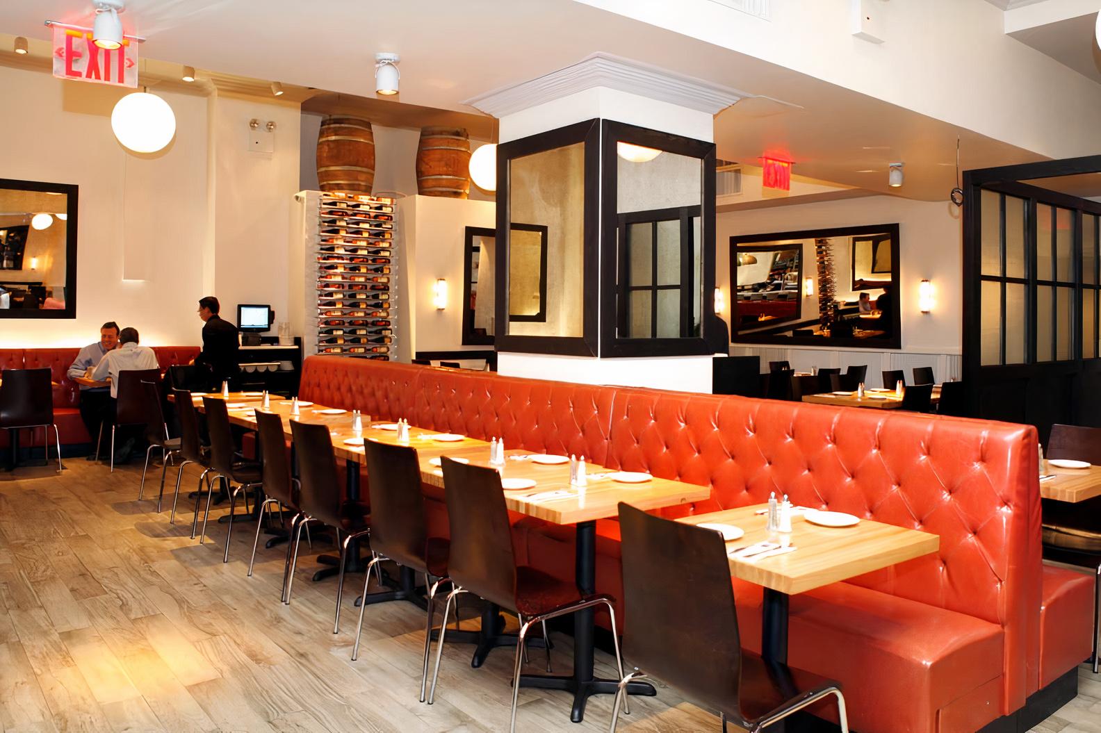 A restaurant dining room with orange tufted banquette seating, wooden tables, and wine shelves at Mr. Broadway.