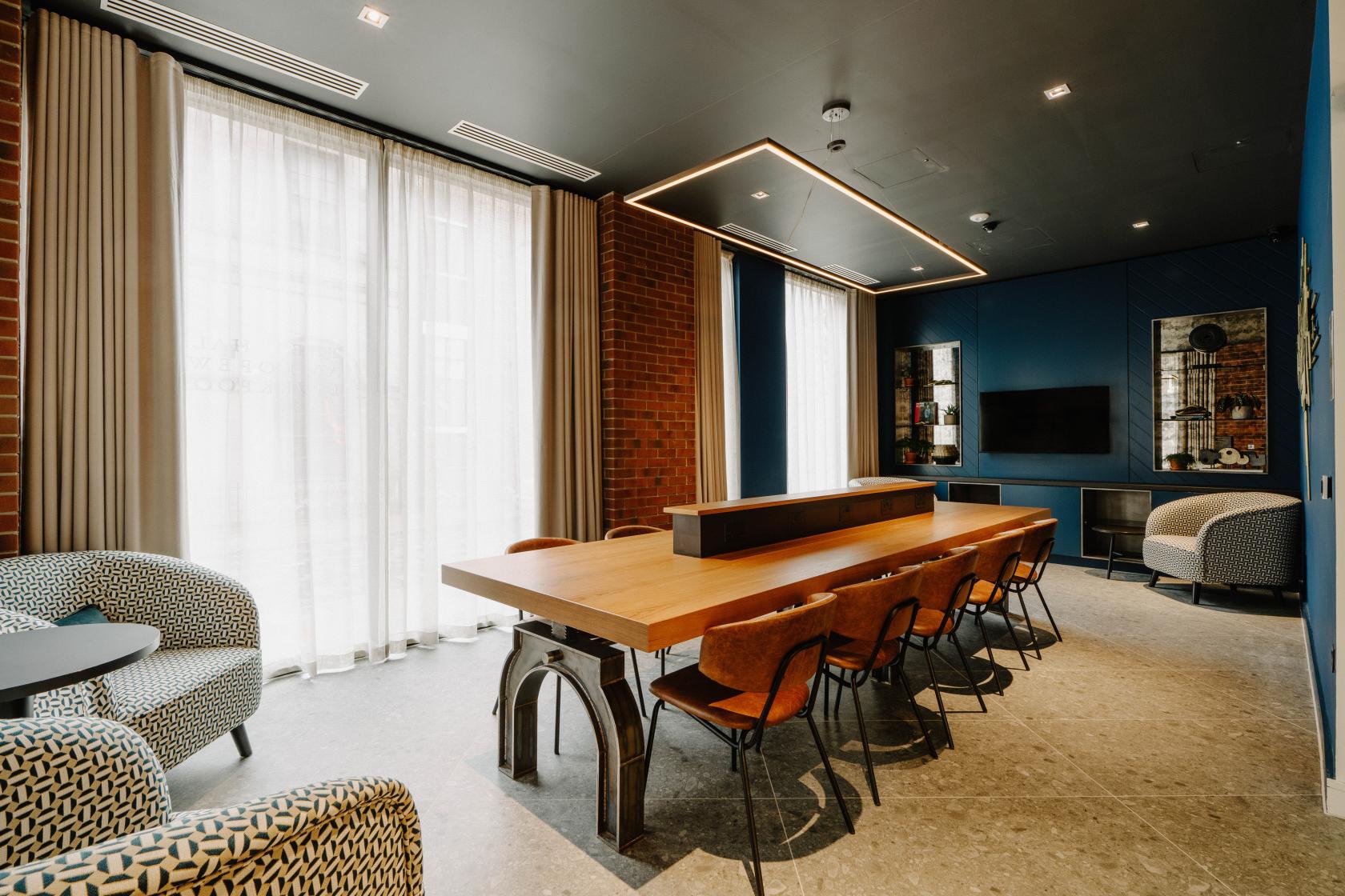 A hotel meeting room with a long wooden table, leather chairs, brick accents, and floor-to-ceiling windows at The Halyard Liverpool, Vignette Collection.