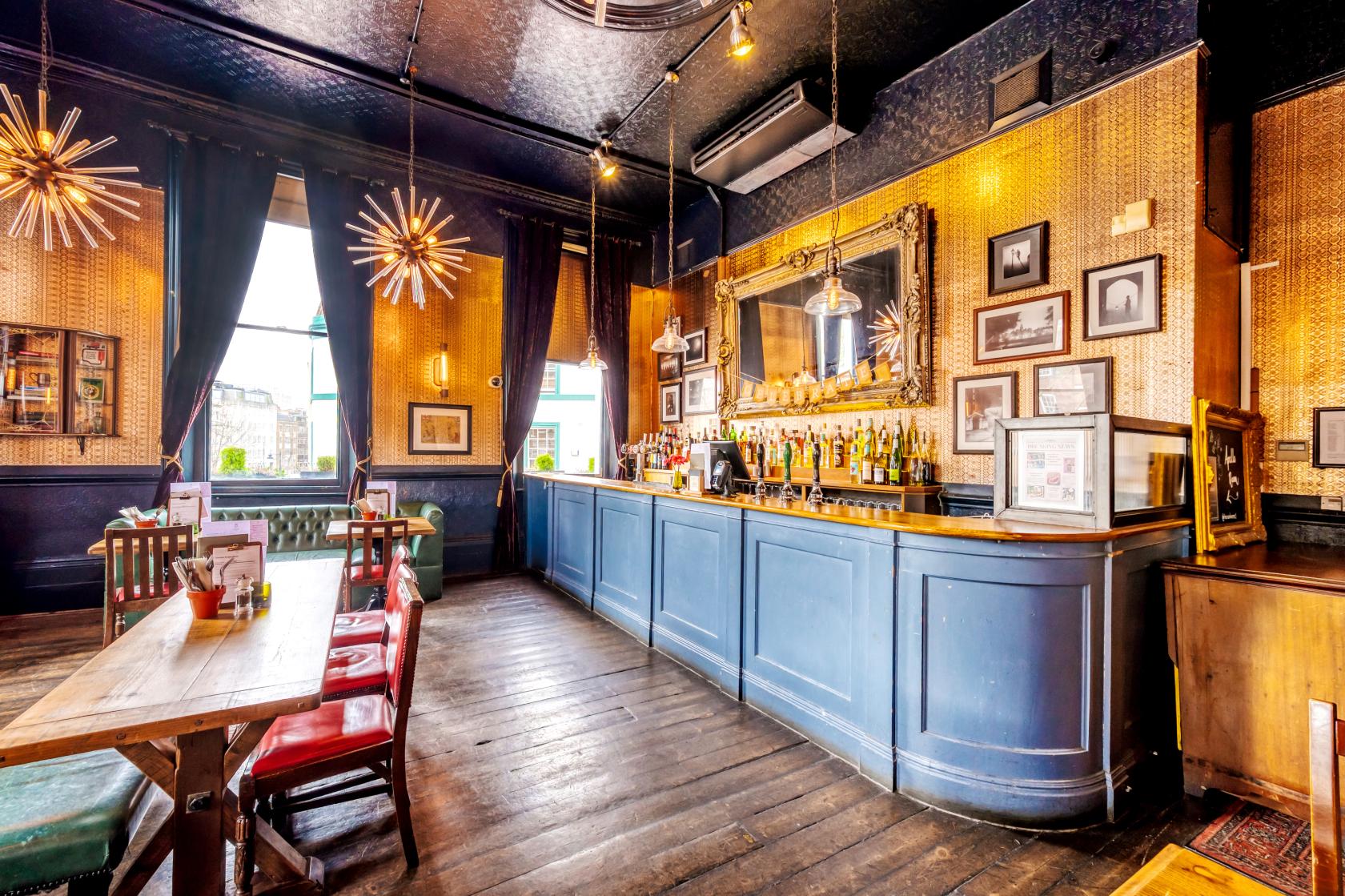 An event space in a pub with vintage wallpaper, wooden floors, and a long blue bar at The Crown Tavern.