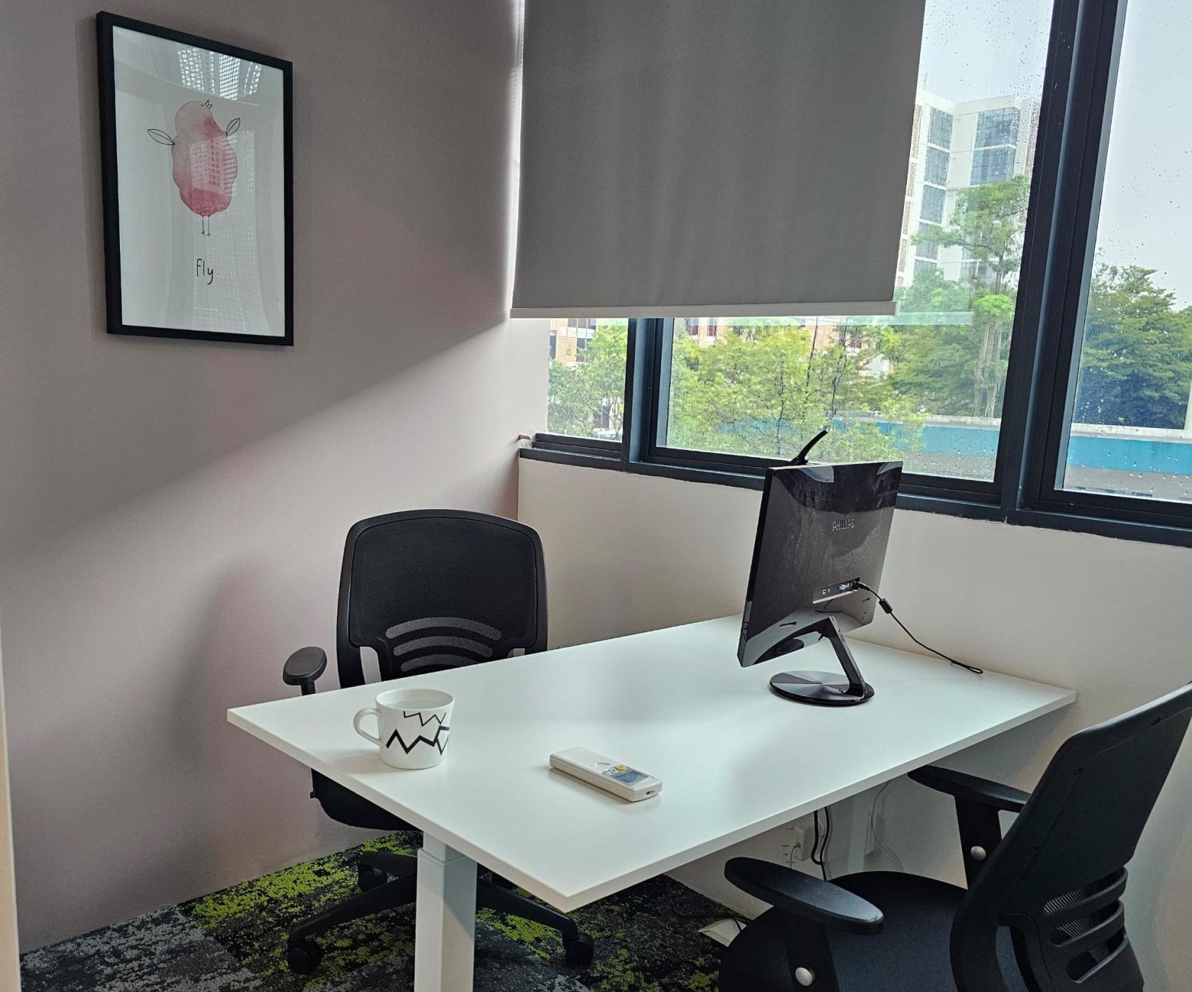 An office space with two chairs, a desk, a computer monitor, and large windows at Dott Cowork.